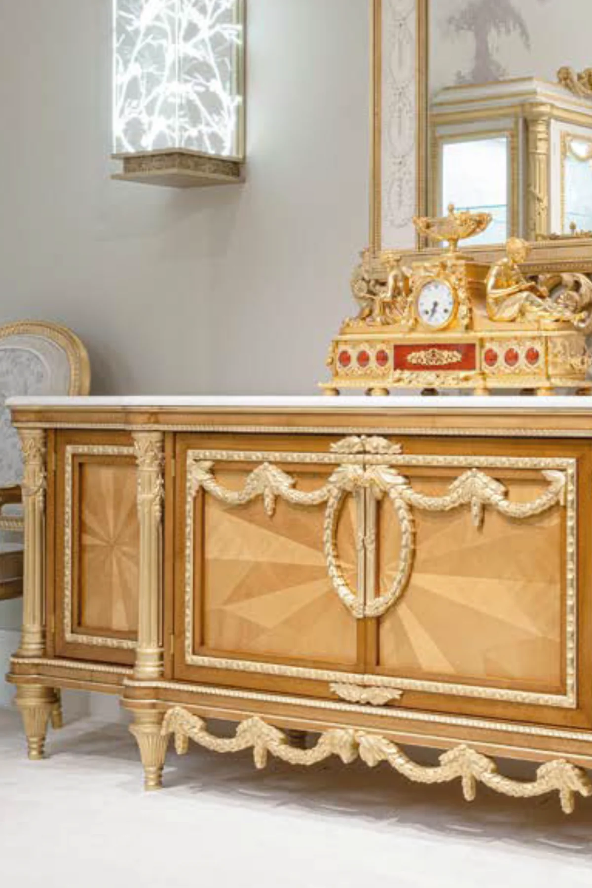 Classic Italian sideboard with marquetry doors and gilded carvings beneath a gold mantel clock