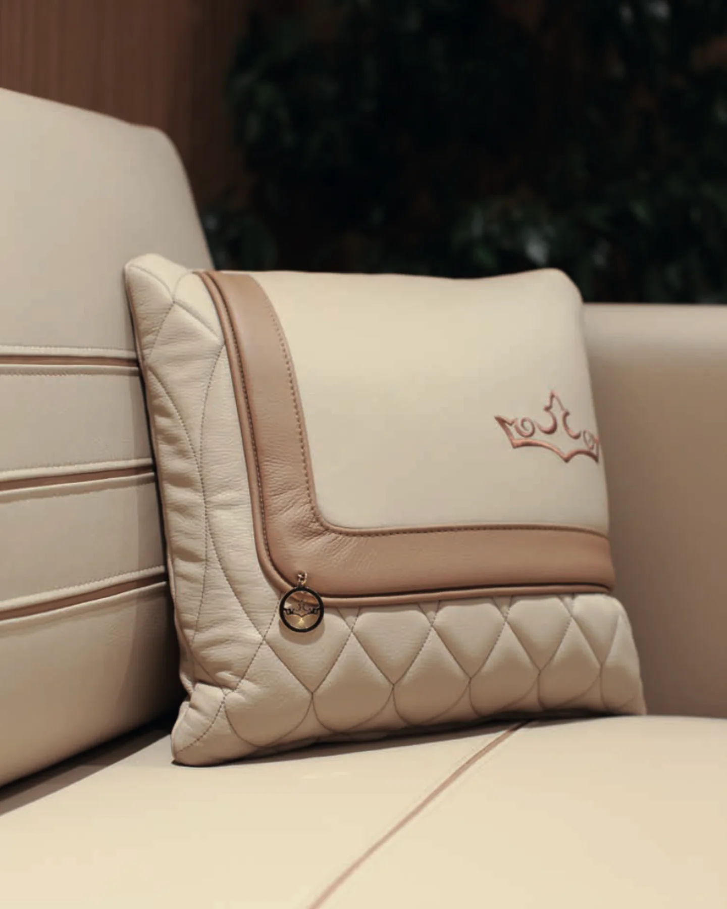 Close-up of a quilted leather cushion with contrast piping and an embroidered crown