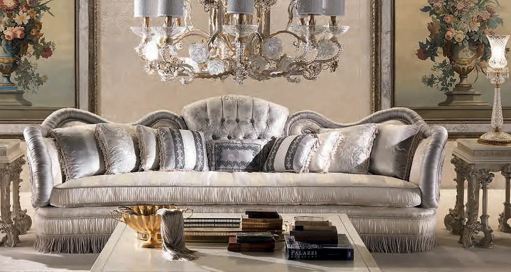 Noblesse catalogue: silver silk tufted sofa with fringed base under a crystal chandelier